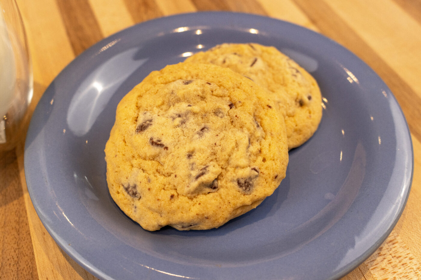 Two Chocolate Chip Cookies stacked on a blue plate atop a wooden table.