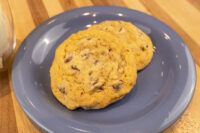 Two Chocolate Chip Cookies stacked on a blue plate atop a wooden table.