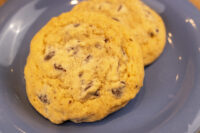 Two golden Chocolate Chip Cookies with cracked tops rest on a gray plate.