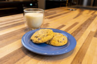 Two Chocolate Chip Cookies on a blue plate beside a glass of milk on a wooden table