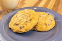 Two Chocolate Chip Cookies stacked on a blue plate with a glass of milk behind them.