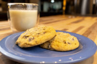 Two Chocolate Chip Cookies stacked on a blue plate beside a glass of milk on a wooden table.