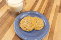 Two Chocolate Chip Cookies on a blue plate with a glass of milk on a wood table