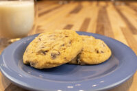 Two Chocolate Chip Cookies on a blue plate beside a glass of milk on a wooden table