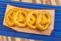 Four golden Czech Soft Pretzel Preclík with coarse salt on a wooden board over blue striped cloth