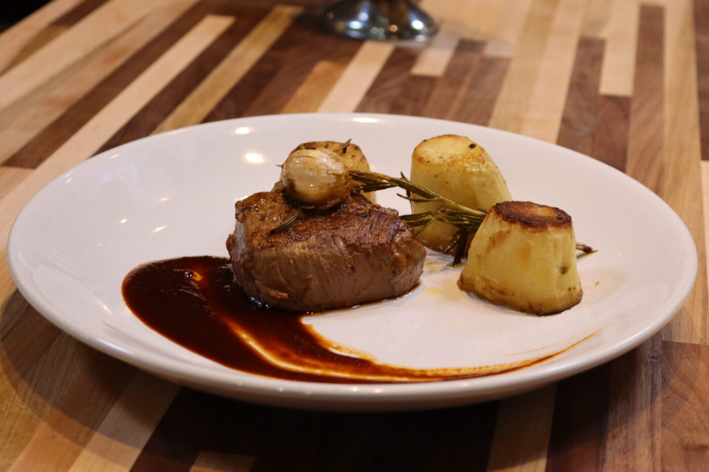 Filet Mignon with Demi-Glace Sauce plated with rosemary, roasted potatoes, and a dark sauce swirl.