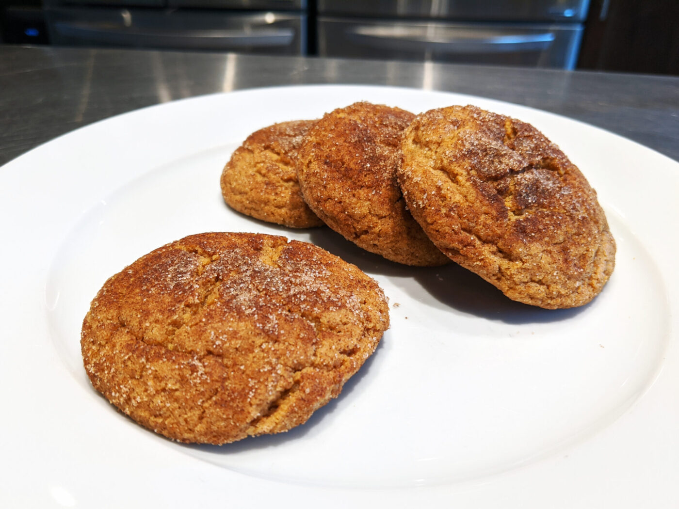 Four Gingersnap Cookies with cracked, sugar-crusted tops on a white plate.
