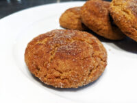 Close-up of sugar-coated Gingersnap Cookies with cracked tops, piled on a white plate.