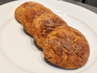 Three golden Gingersnap Cookies with crackled, sugar-coated tops arranged in a row on a white plate.
