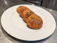 Two golden-brown Gingersnap Cookies with cracked, sugared tops on a white plate.