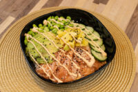 Poke Bowl with Salmon in a black dish with salmon, avocado, mango, cucumber, and spicy mayo.