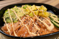Poke Bowl with Salmon in a black bowl with salmon, avocado, mango, cucumber, sesame seeds, and spicy mayo.