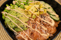 Poke Bowl with Salmon topped with salmon, avocado, mango, cucumber, edamame, sesame seeds and spicy mayo drizzle
