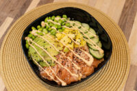 Poke Bowl with Salmon topped with avocado, edamame, mango, cucumber, sesame seeds, and spicy mayo drizzle