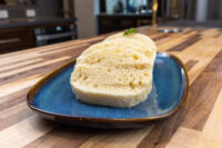 Sliced houskový knedlík with bubbly interior and herb garnish on a blue plate.