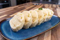 Sliced houskový knedlík rounds on a blue plate, garnished with a parsley leaf.