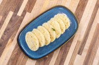 Sliced rounds of houskový knedlík with a spongy, holey texture, fanned on a dark blue oval plate.