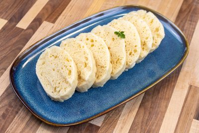 Sliced houskový knedlík rounds with airy texture on a blue oval plate, garnished with herb.