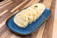 Sliced houskový knedlík rounds with airy crumb on a blue oval plate, garnished with parsley.