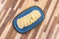 Sliced houskový knedlík rounds fanned on a blue oval plate with a parsley garnish on a wood table.