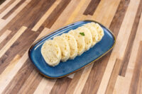 Sliced rounds of houskový knedlík arranged on a blue oval plate with a herb garnish.