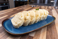 Sliced houskový knedlík rounds on a blue plate, spongy crumb visible, garnished with parsley.