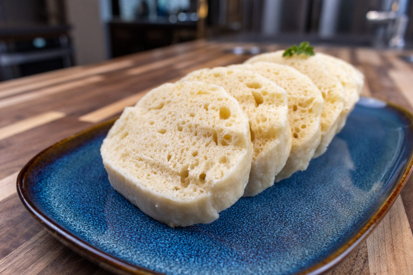 Sliced houskový knedlík with visible air holes, garnished with herb, on a blue ceramic plate.