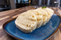 Sliced houskový knedlík with visible air holes, garnished with herb, on a blue ceramic plate.