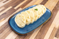 Sliced houskový knedlík rounds with airy holes on a blue oval plate, garnished with a herb leaf.
