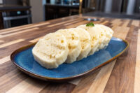 Sliced houskový knedlík rounds fanned on a blue plate, showing spongy, porous texture, garnished with herb.