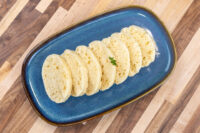 Sliced houskový knedlík fanned on a dark blue plate, garnished with a small herb sprig.