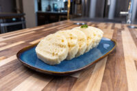Sliced houskový knedlík with a spongy, holed texture on a blue oval plate with herb garnish.