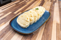 Sliced houskový knedlík rounds with visible air pockets, fanned on a blue oval plate on a wooden table.
