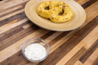 Small glass bowl of Garlic Dipping Sauce for Pretzels with herb flecks, beside a seeded pretzel.