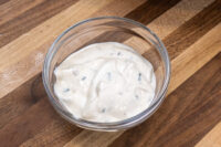 Glass bowl of Garlic Dipping Sauce for Pretzels, creamy with dark herb flecks, on a wood surface.