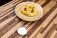 A small glass bowl of Garlic Dipping Sauce for Pretzels with visible chive flecks, set beside a seasoned pretzel.
