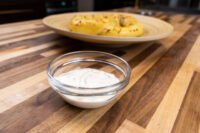 Glass bowl of Garlic Dipping Sauce for Pretzels with herb flecks, pretzels on a plate behind it
