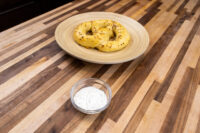 Small glass bowl of Garlic Dipping Sauce for Pretzels with herb flecks, next to a plate of pretzels on a wood table
