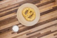 A small glass bowl of Garlic Dipping Sauce for Pretzels next to a mustard-seed pretzel on a wooden table.