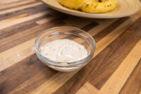 Glass bowl of Garlic Dipping Sauce for Pretzels, a creamy dip flecked with chives, on a wood table.