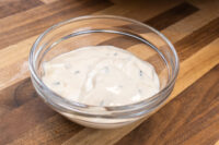 Glass bowl of creamy Garlic Dipping Sauce for Pretzels with visible chive flecks on a wooden surface.