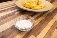 Glass bowl of Garlic Dipping Sauce for Pretzels with herb flecks, pretzels on wooden plate behind.