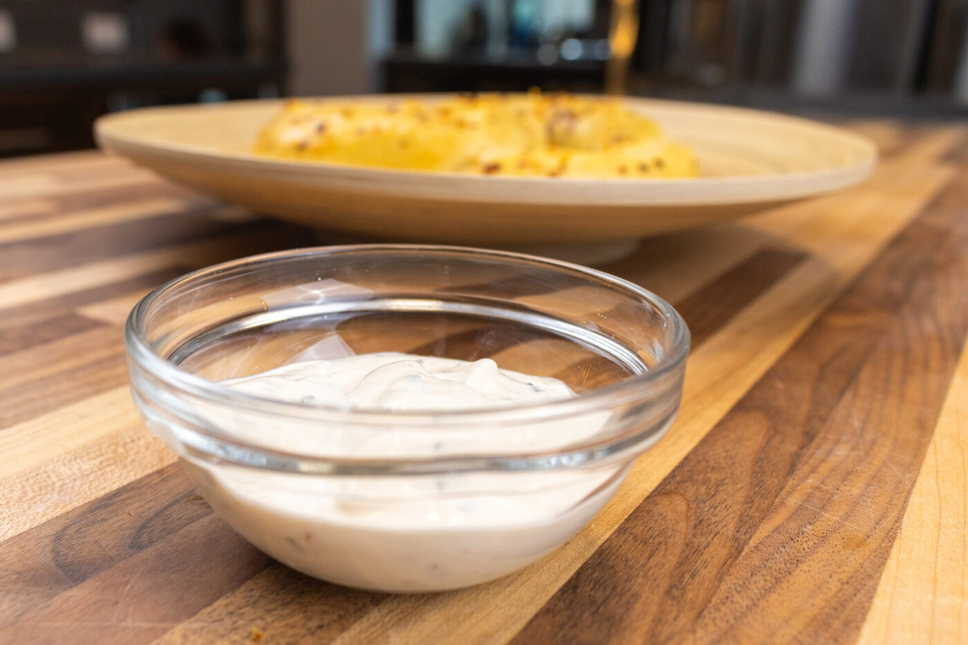 Glass bowl of Garlic Dipping Sauce for Pretzels, creamy with dark chive flecks, on a wood table.