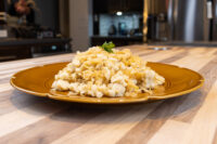 Mounded Halušky with Sauerkraut on a gold plate, topped with a fresh herb sprig, on a wooden countertop