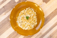 Plated Halušky with Sauerkraut, pale shredded dumplings topped with parsley on a mustard ceramic plate.