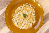 Overhead view of Halušky with Sauerkraut in a mustard-yellow ceramic bowl, showing soft potato dumplings mixed with shredded sauerkraut and a parsley garnish, set on a wooden surface.