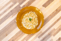 Halušky with Sauerkraut on a scalloped mustard plate, garnished with chopped herbs, set on striped wood.