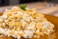 A gold-rimmed plate piled with soft Halušky with Sauerkraut, the pale dumplings mixed with golden strands and topped with a sprig of parsley.