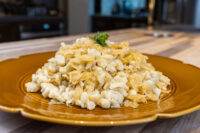 Mound of Halušky with Sauerkraut topped with a parsley sprig on a mustard-yellow scalloped plate.