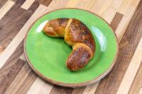Golden Loupáčky Czech Poppy Seed Crescent topped with poppy seeds on a green ceramic plate.
